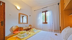 Una camera da letto ordinata con un letto, un comodino, uno specchio e una finestra con tende.
