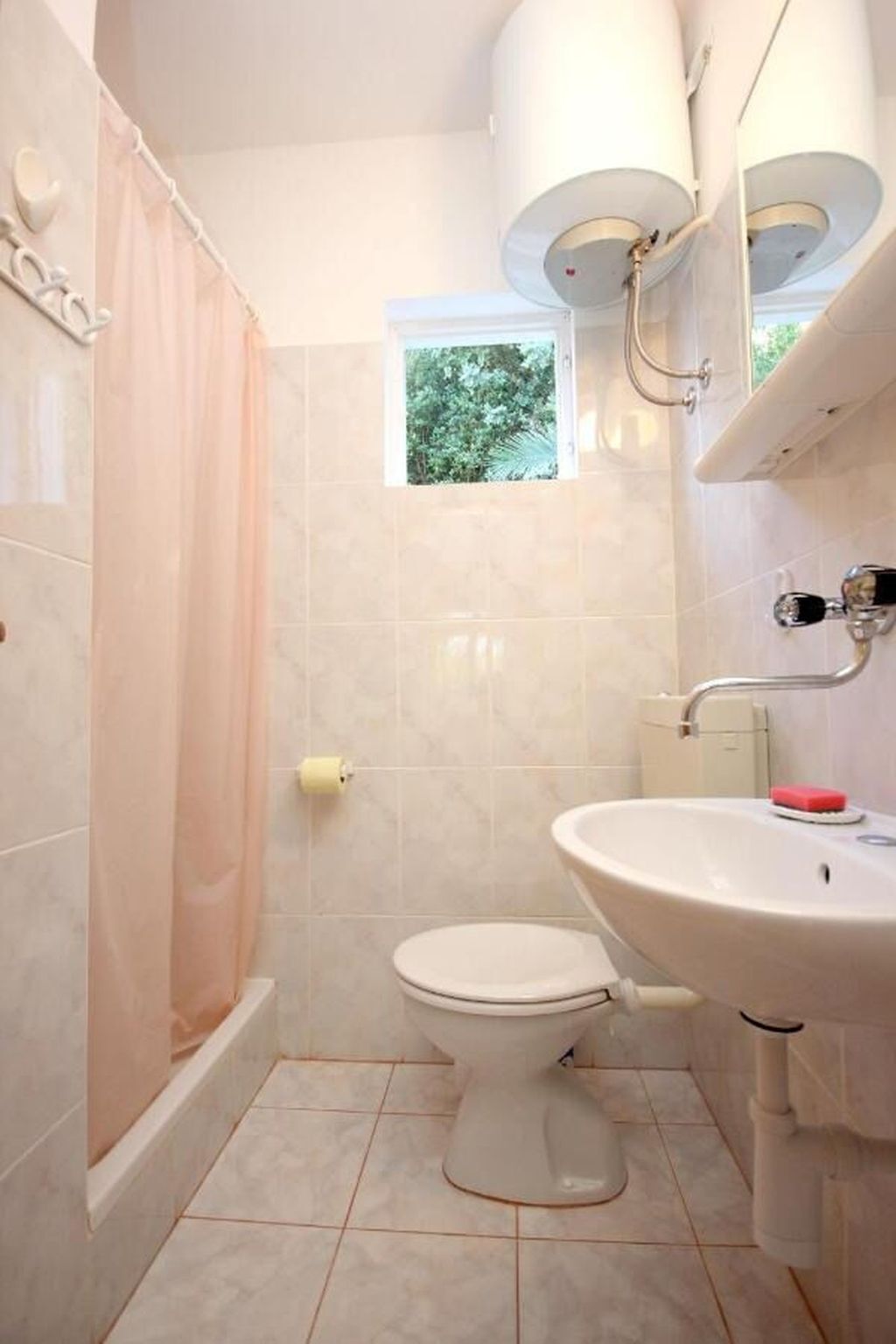A bathroom with a toilet, sink, shower, and a small window.