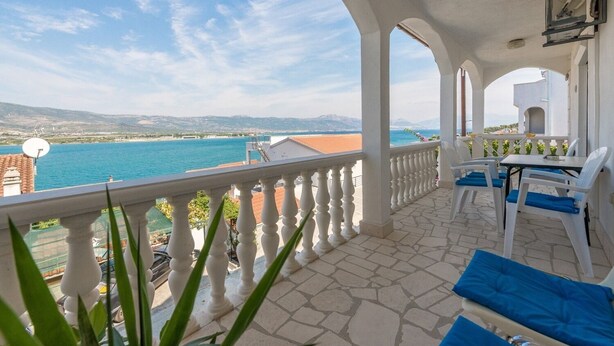 Ein Balkon mit Meerblick, weißen Säulen und einem Tisch mit Stühlen.