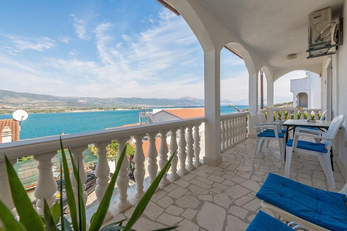 Un balcon avec vue sur la mer, des colonnes blanches et une table avec des chaises.