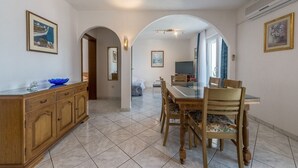 Ein geräumiger Essbereich mit großem Tisch und Stühlen, einem Holzschrank und einem Fernseher im Hintergrund.