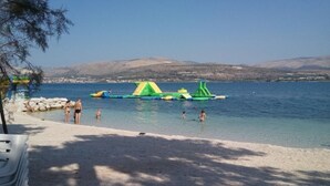 Ein Strand mit klarem Wasser, sandigem Ufer und aufblasbaren Wasserspielgeräten.