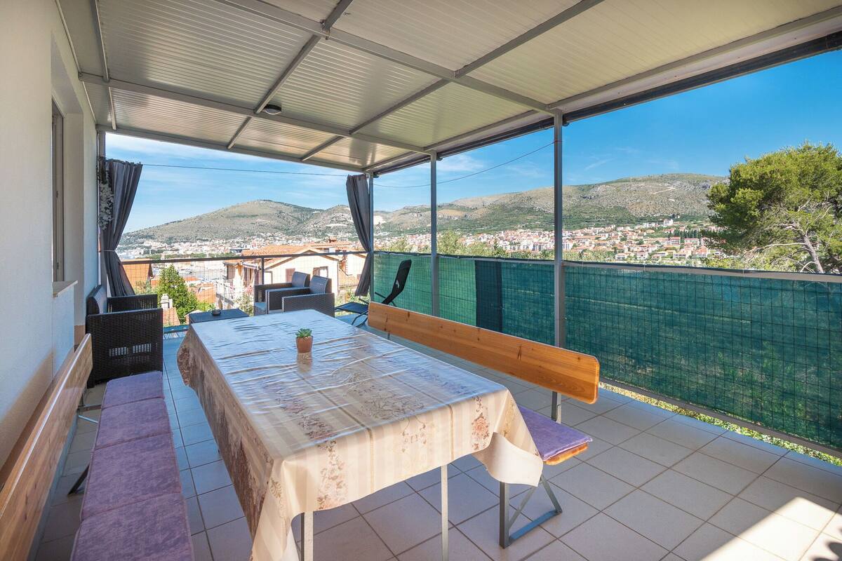 Un balcon abrité, équipé d’une table, de bancs et offrant une vue sur la ville et les collines.