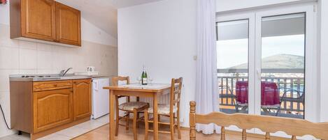 A compact kitchen with wooden cabinets, a dining table with chairs, and a balcony with a view.