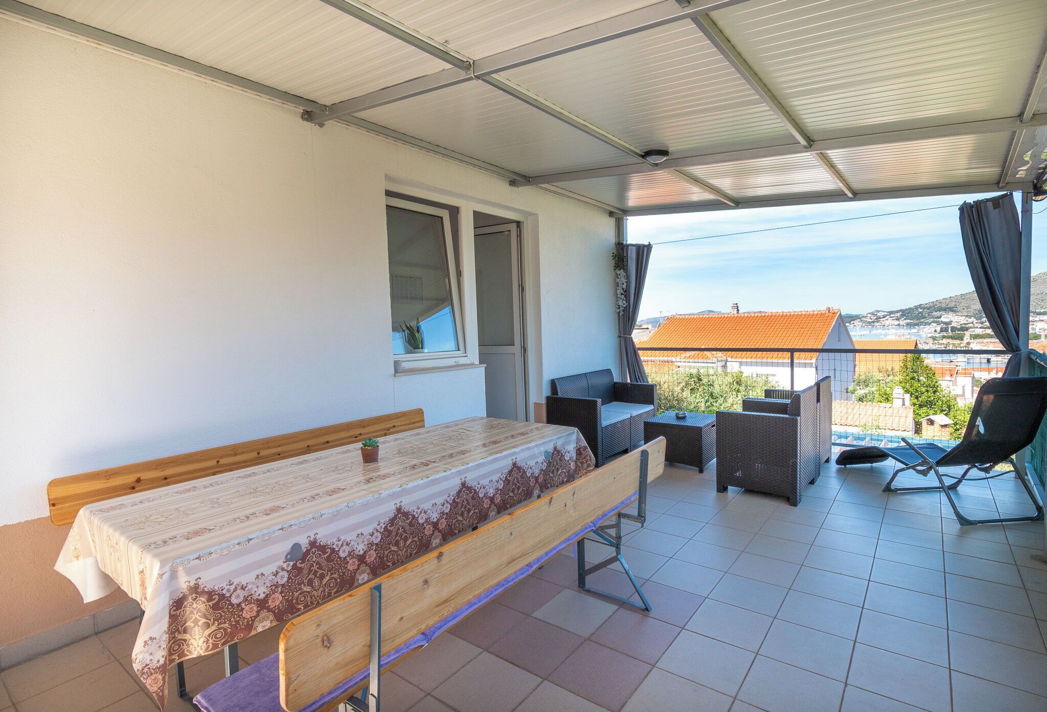 A covered outdoor patio with a table, benches, and chairs, overlooking a residential area.