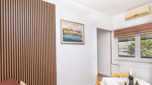 Ein Zimmer mit einer Wand aus Holzleisten, einem gerahmten Gemälde einer Küstenlandschaft, einem Esstisch mit Stühlen und einem Fenster mit Blick auf Grünflächen.