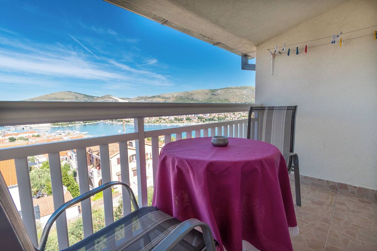 Un balcon avec une table et des chaises, donnant sur un plan d’eau et une ville.