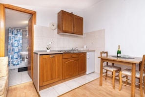 A compact kitchen with wooden cabinets, a sink, a dishwasher, and a dining table with chairs. - Apartments Mara (Trogir)