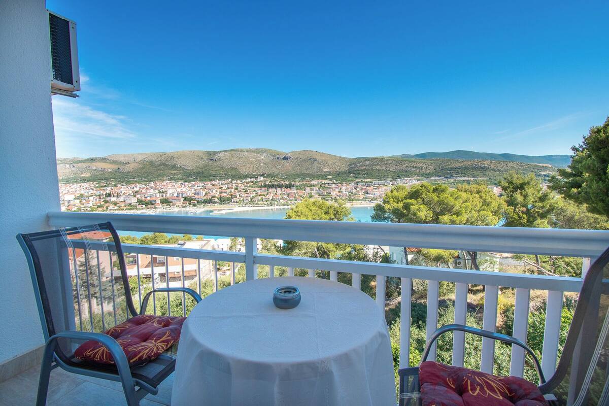 Un balcon avec une table et des chaises, d’où l’on a vue sur la ville et les collines.