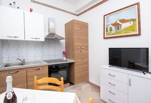 Une cuisine moderne avec des armoires blanches, un four encastré, une chaise en bois et un téléviseur posé sur une armoire blanche.