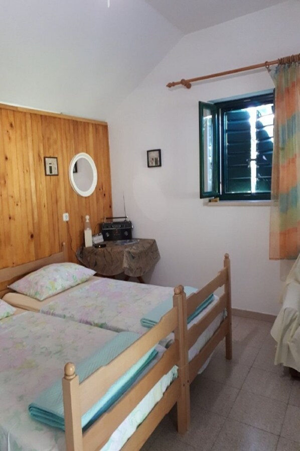 Une chambre à coucher avec deux lits en bois, une armoire en bois, un miroir rond, une radio et une fenêtre avec des rideaux.
