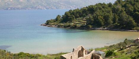 A coastal landscape with a clear view of a body of water, a small island with trees, and a stone ruin in the foreground.