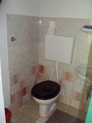 A small bathroom with a toilet, a sink, and a toilet paper holder. - House Lidija (Postira)
