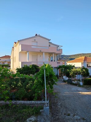 A two-story residential building with a balcony, surrounded by a garden with various plants and a gravel driveway. - Apartment Slaven (Marina)