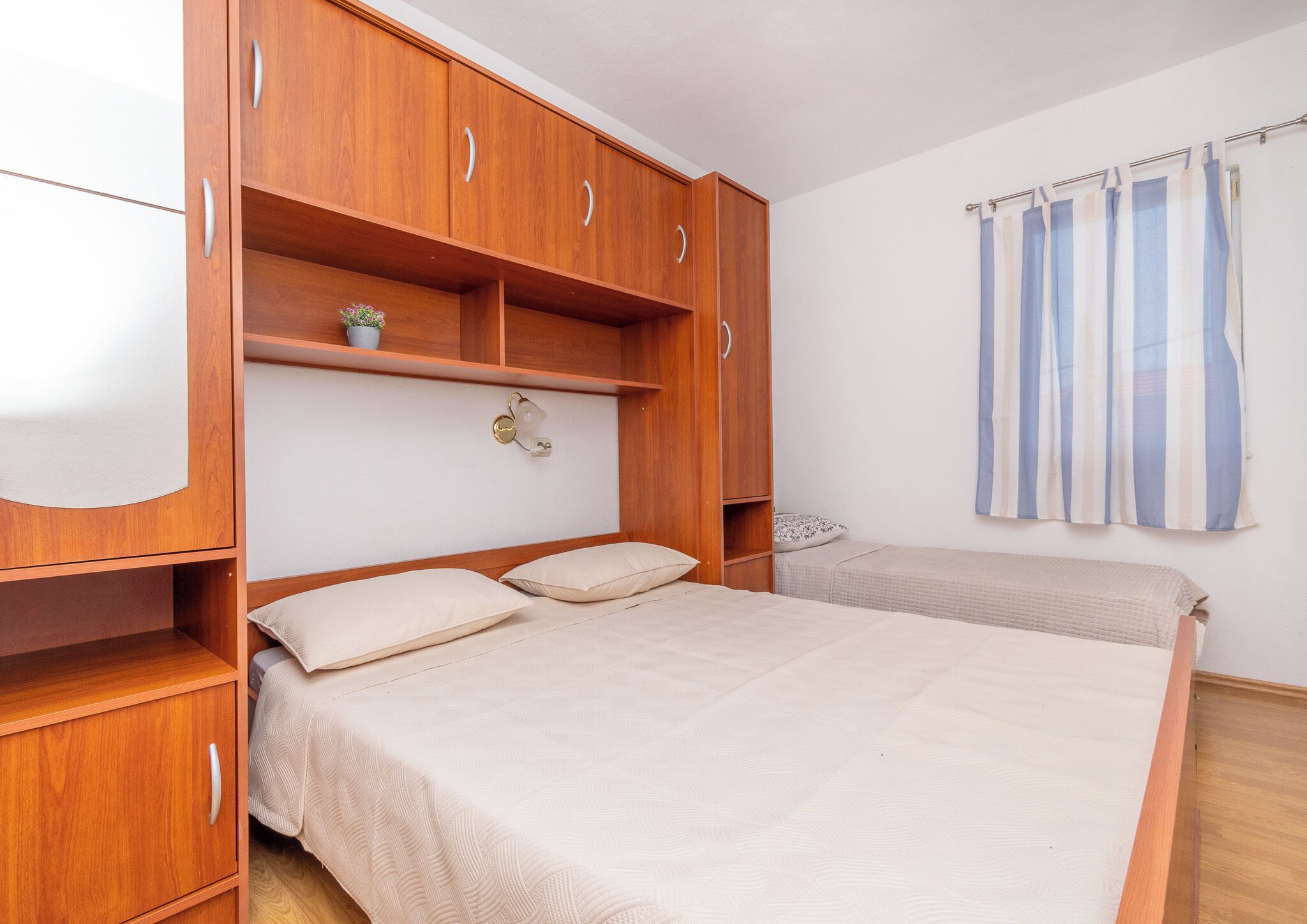 A bedroom with a bed, wooden wardrobe, and a window with curtains.