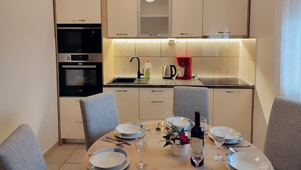 A modern kitchen with built-in appliances, a dining area with a table set for four, and a small bar area. - Apartment Slaven (Marina)
