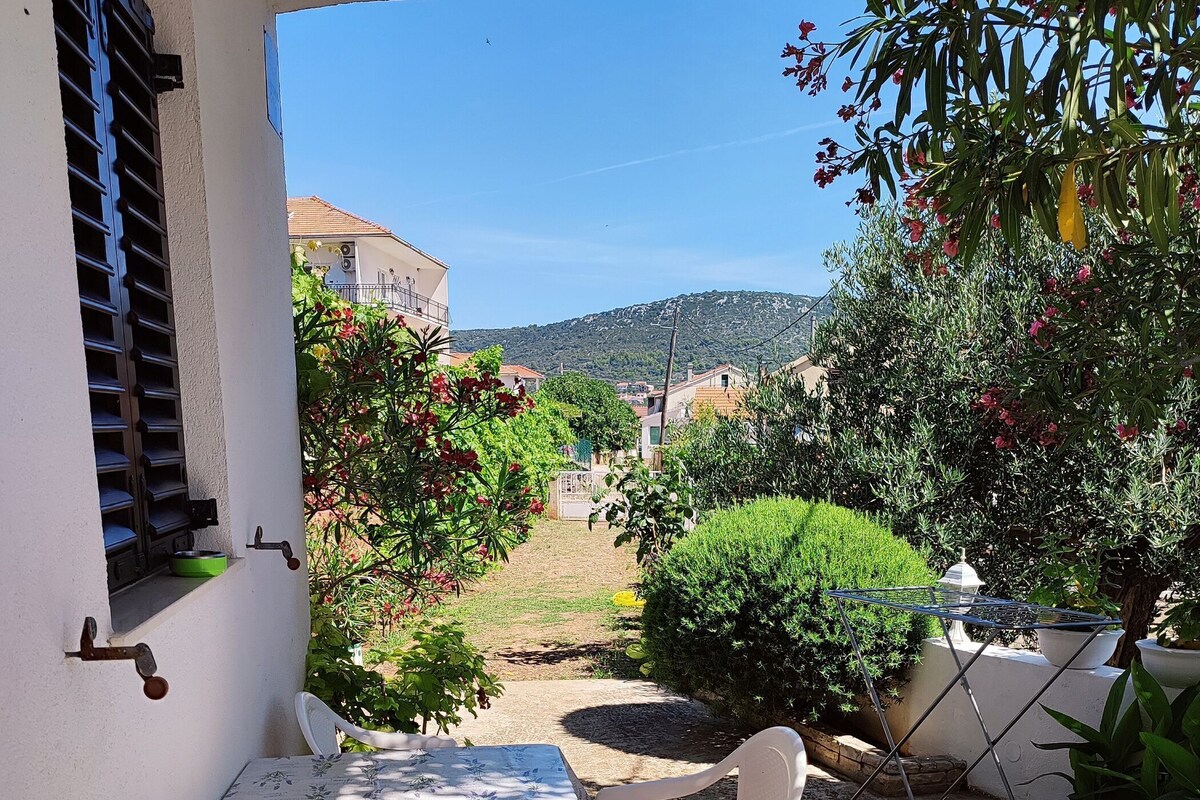 Eine Terrasse im Freien mit Tisch und Stühlen, umgeben von viel Grün und Blick auf das Dorf im Hintergrund.