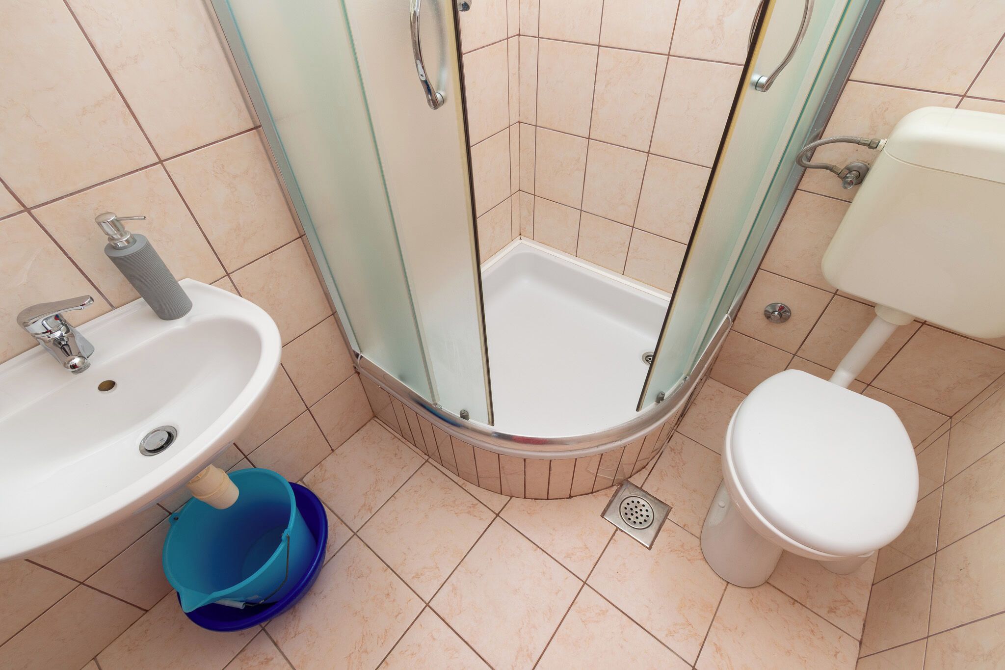 Un bagno con doccia, lavandino, WC e un secchio blu.