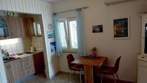 Eine kompakte Küche mit Essbereich, inklusive einem Holztisch, Stühlen, einem kleinen Schrank und einem Fenster mit Vorhängen.
