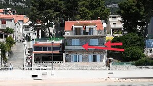 Ein Küstenhaus mit einer Steinfassade, einem roten Ziegeldach und einem Balkon.