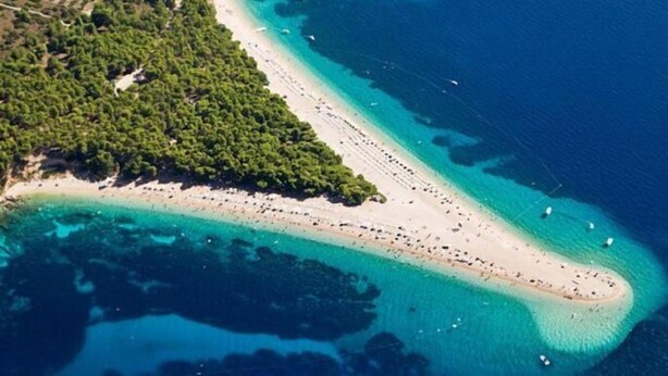 Eine Vogelperspektive zeigt eine Küstenlandschaft mit einem weiten Sandstrand, Booten und dichter Vegetation.