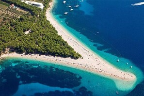 Vista aérea de una zona costera con una extensa playa, barcos y vegetación densa.
