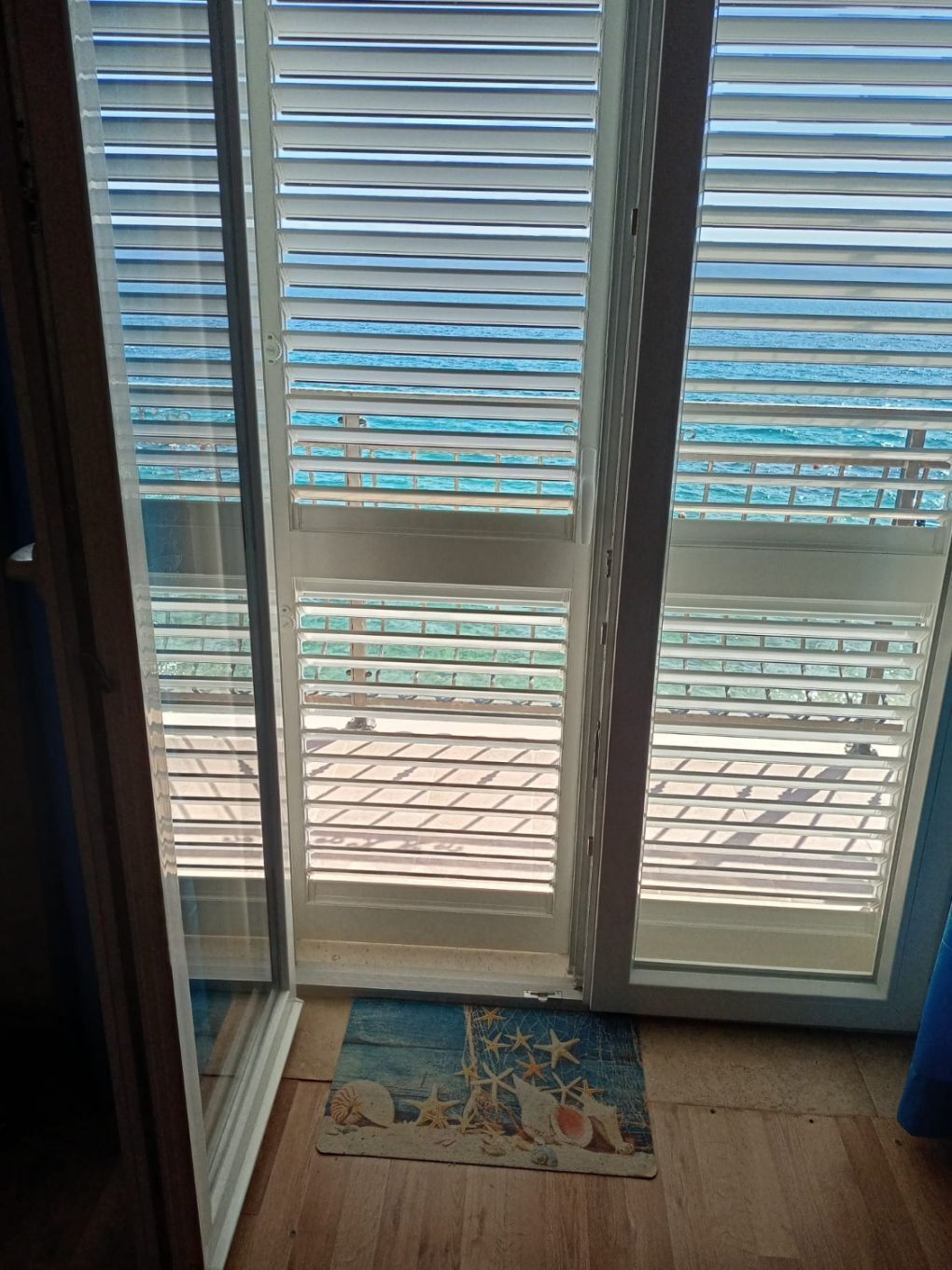 A room with a sliding glass door leading to a balcony with horizontal blinds.