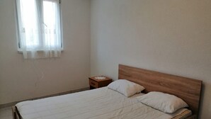 A single bed with a wooden headboard in a room with white walls and a window with sheer curtains. - Apartments Branko (Vis)