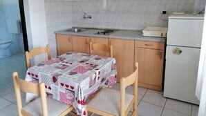 A small kitchen with a table set for two, wooden chairs, a refrigerator, and a sink. - Apartments Branko (Vis)