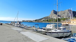 A marina with several boats docked, a rocky hill in the background, and a clear blue sky. - Apartment Iva (Omis)