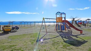 A playground with swings and slides, a yellow vehicle, and a clear view of the sea. - Apartment Iva (Omis)