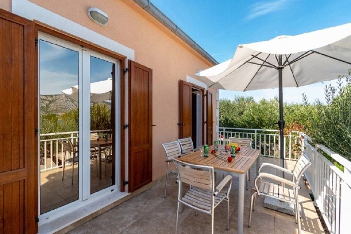 A patio with a table and chairs, a white umbrella, and a sliding glass door.