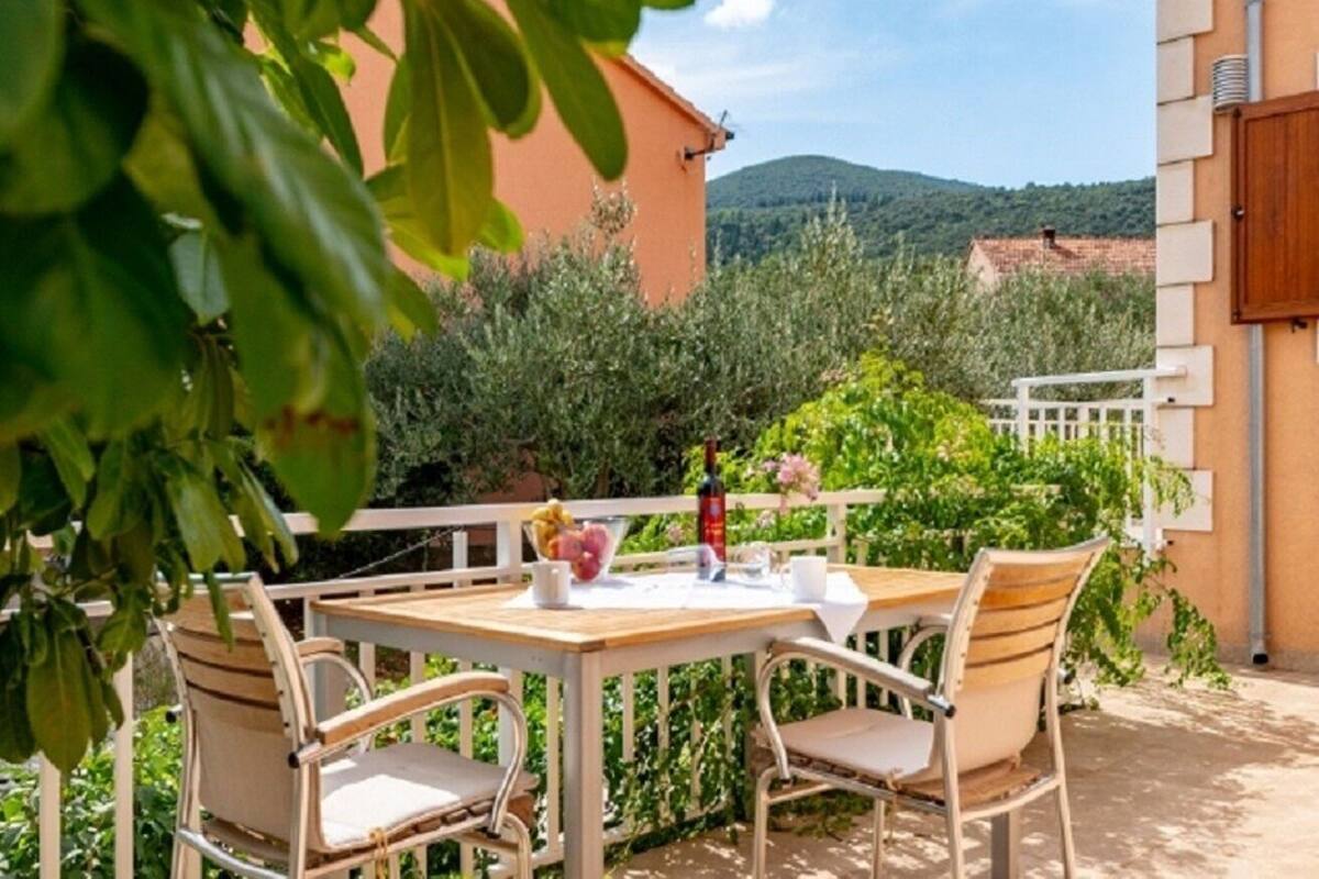 An outdoor patio with a table and chairs, surrounded by greenery and a view of hills.