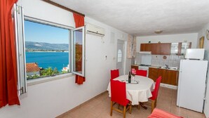 A compact kitchen with a dining area, a view of the sea, and a balcony with red curtains. - Apartment Marija (Trogir)