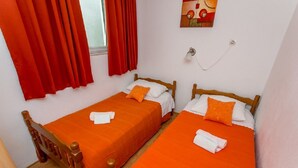 A room with two single beds, each with an orange bedspread and white pillows, a wooden headboard, and a red curtain. - Apartment Marija (Trogir)