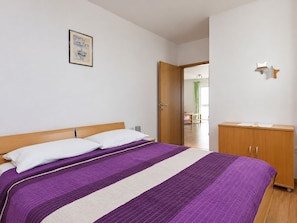 A bedroom with a bed, a wooden wardrobe, a door leading to another room, and a framed picture on the wall. - Apartment Ljilja (Hvar)