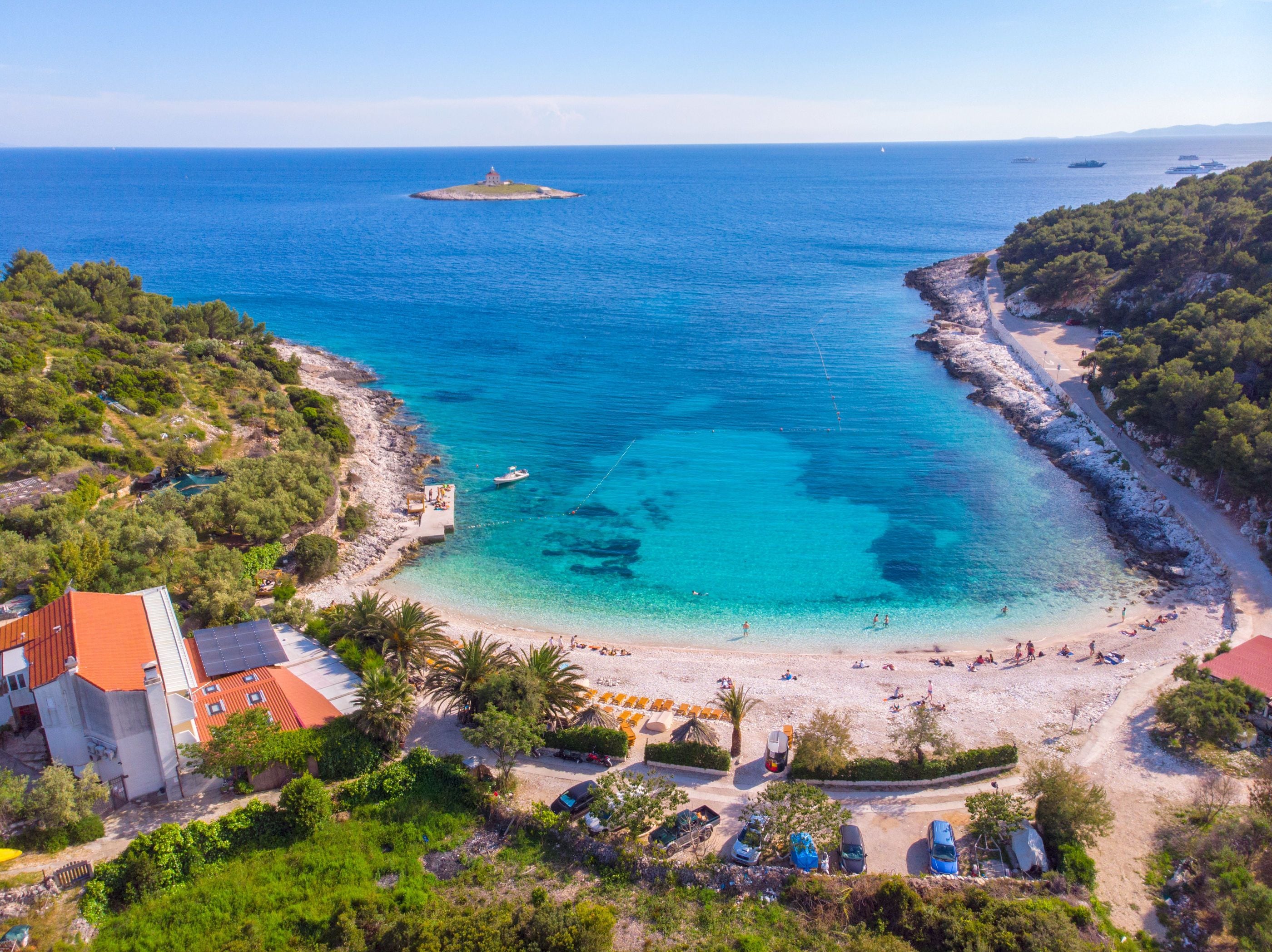 A coastal area with a beach, a small island, and a building with a red roof.