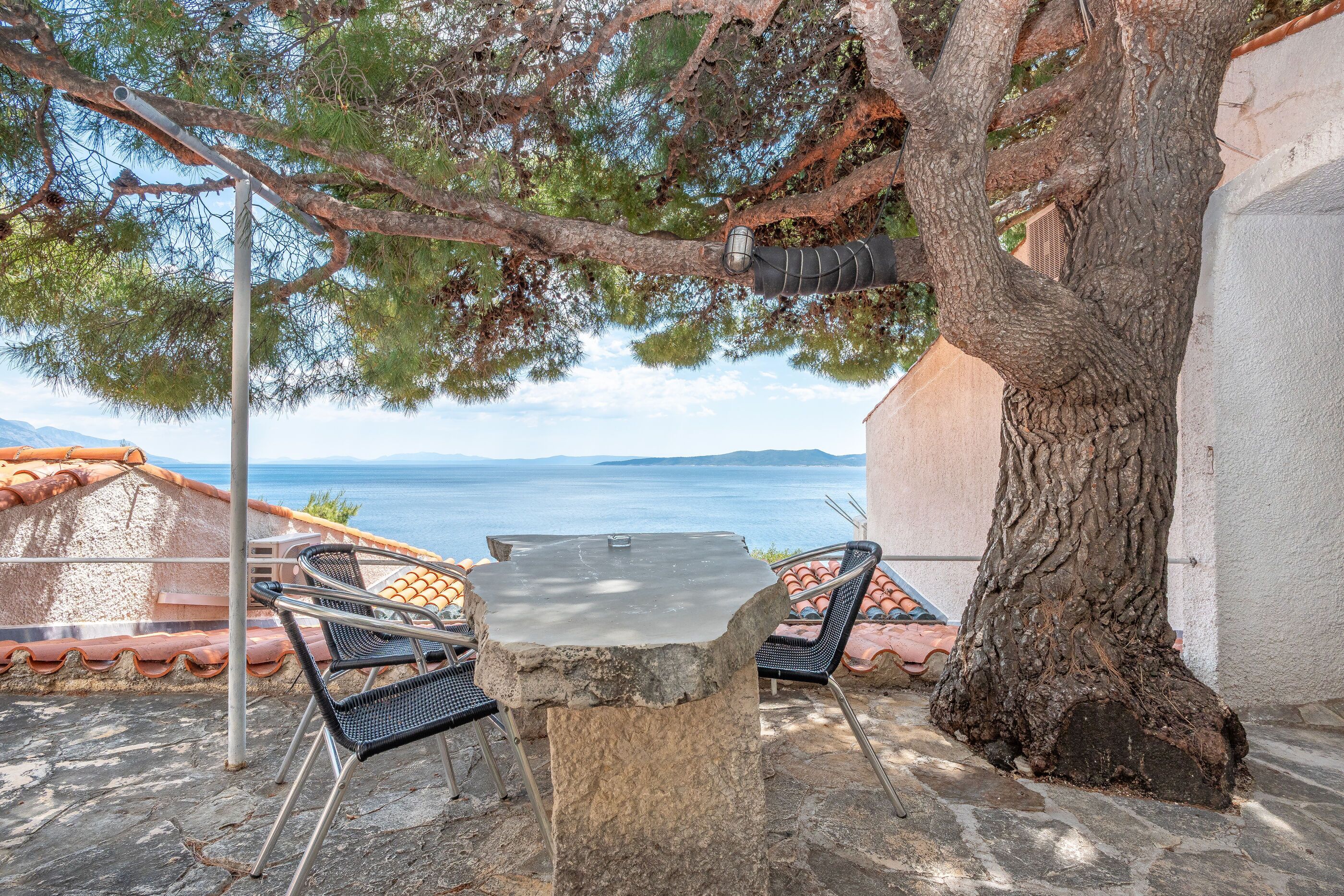 Ein Steintisch mit Stühlen, ein Baum und Meerblick.