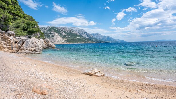 A beach with clear water, rocky terrain, and mountains in the background. - Apartments Marko (Omis)