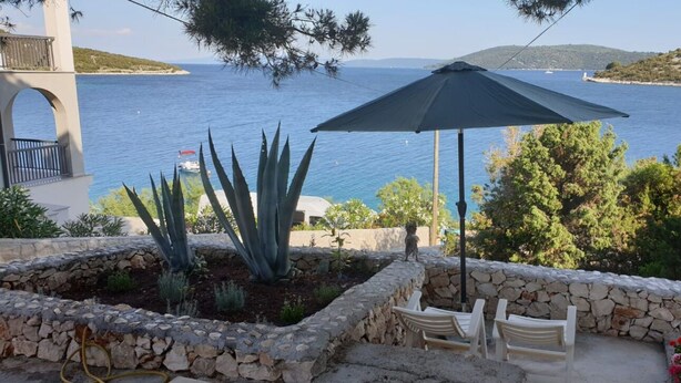 Un patio con un muro in pietra, un ombrellone e vista sul mare.