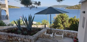 A patio with a stone wall, an umbrella, and a view of the sea. - Apartment Natad (Marina)