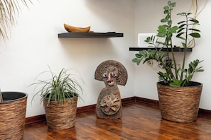 Una esquina con tres plantas en macetas, una escultura de madera y un estante con un cuenco.