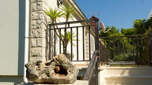 A stone wall with a rock, a metal gate, and a staircase leading to a building with a satellite dish. - Apartments Dijana (Blato)