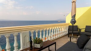A balcony with a view of the sea, a sofa, a table with a bottle and glasses, and an umbrella. - Apartments Dijana (Blato)