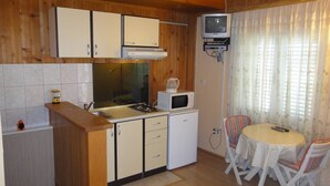 Una cocina compacta con estufa, microondas y armarios, un refrigerador pequeño y un comedor con mesa y sillas.