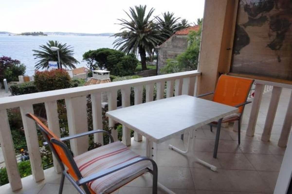 Un balcon avec une table blanche et deux chaises, donnant sur une étendue d’eau et une zone verdoyante.