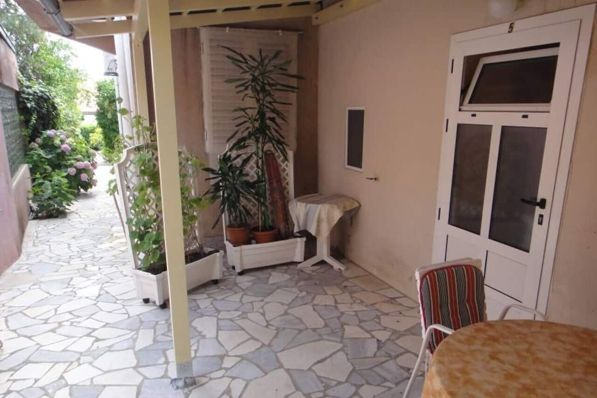 Une terrasse couverte avec un sol en pierre, des plantes en pot, une table et une chaise.