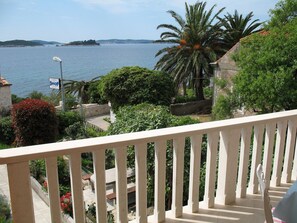 Ein Balkon mit Blick auf ein Gewässer, Palmen und einem Schild für ein Geschäft.