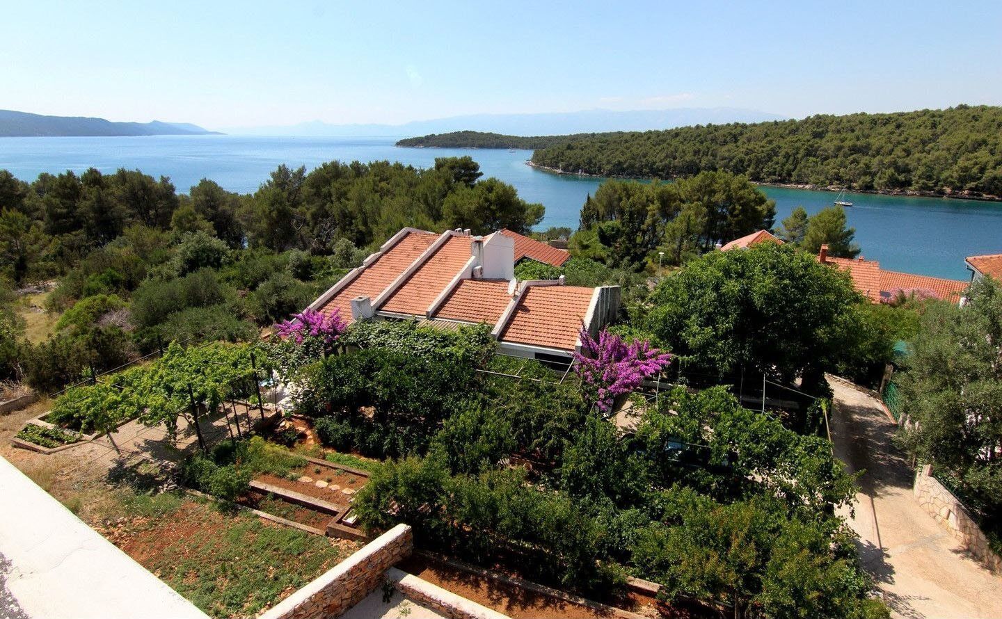 Ένα παραθαλάσσιο ακίνητο με σκαλωστά δώματα, έναν κήπο με λουλούδια σε αποχρώσεις του μωβ και θέα στη θάλασσα και στους λόφους.
