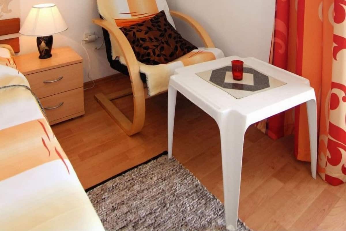 A small, well-lit room with a wooden chair, a small table, a lamp, and a bed.